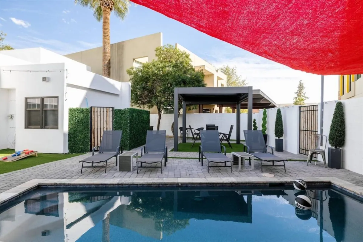 A sun-dappled pool area with inviting lounge chairs, a shaded pergola, and open patio space perfect for relaxing, mingling, or enjoying a refreshing swim. The scene suggests both daytime and evening use, with flexible spaces for group fun.