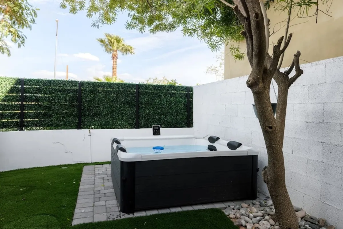 A tranquil hot tub nestled among lush greenery and palm trees, with warm sunlight filtering through. The scene exudes relaxation, perfect for unwinding at sunset or enjoying a starlit evening outdoors.