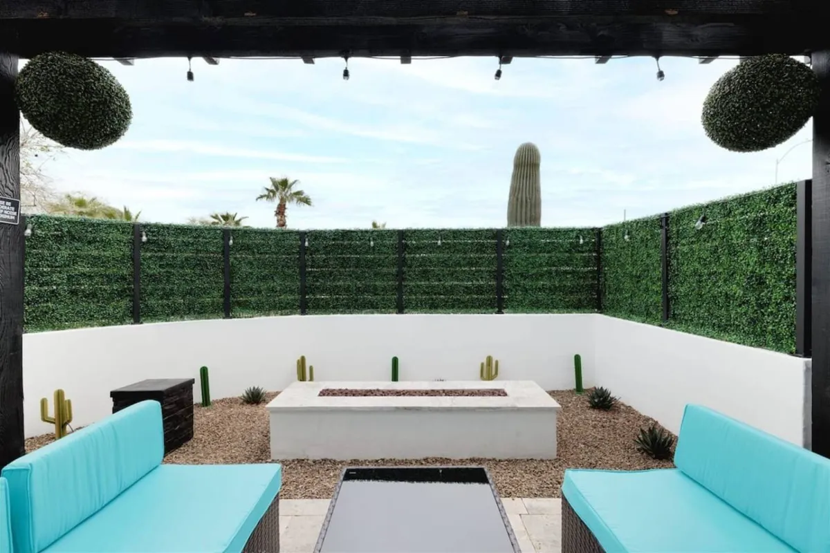 A stylish outdoor area with turquoise lounge seating, a fire pit centerpiece, and surrounding greenery and cacti. The space is designed for relaxing, socializing, and enjoying cozy evenings, with a backdrop perfect for both daytime and nighttime gatherings.