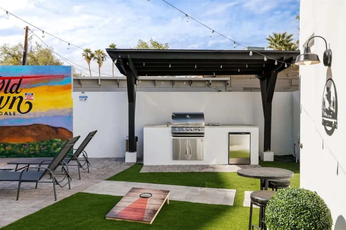An outdoor kitchen equipped with modern amenities, complemented by a colorful mural and a spacious seating area. The scene is set for group barbecues or al fresco dining, with ample room for everyone to gather under the open sky as evening approaches.