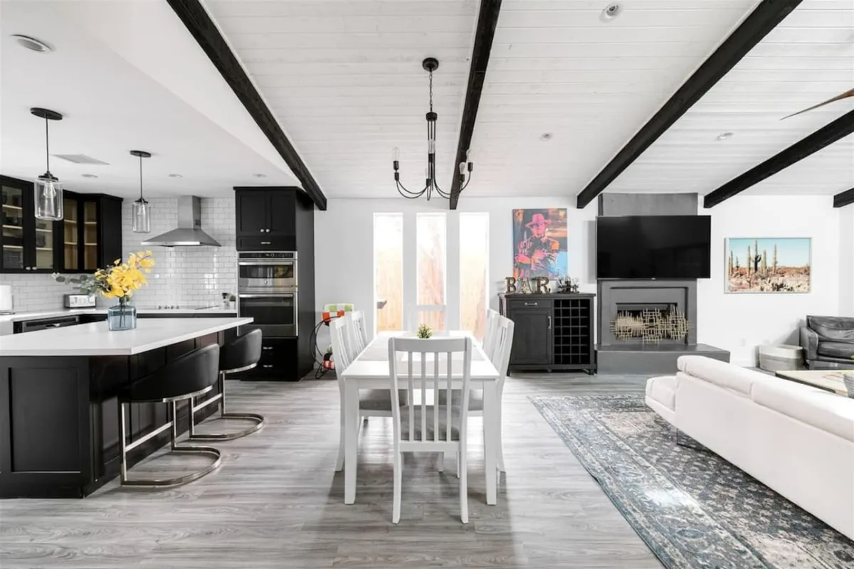 An inviting open-plan kitchen and dining space that seamlessly connects a kitchen island to a dining table. The scene includes a cozy fireplace, contemporary wall art, and comfortable seating, creating an atmosphere ideal for socializing, dining, and relaxation.