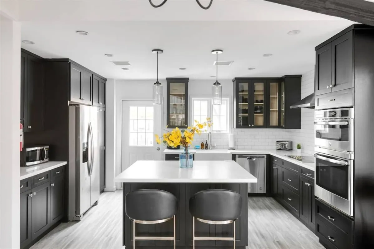 A contemporary kitchen featuring a central island adorned with a flower arrangement, sleek black cabinetry, and stainless steel appliances. The space is styled for both functionality and warmth, with ample room for cooking and hosting gatherings.