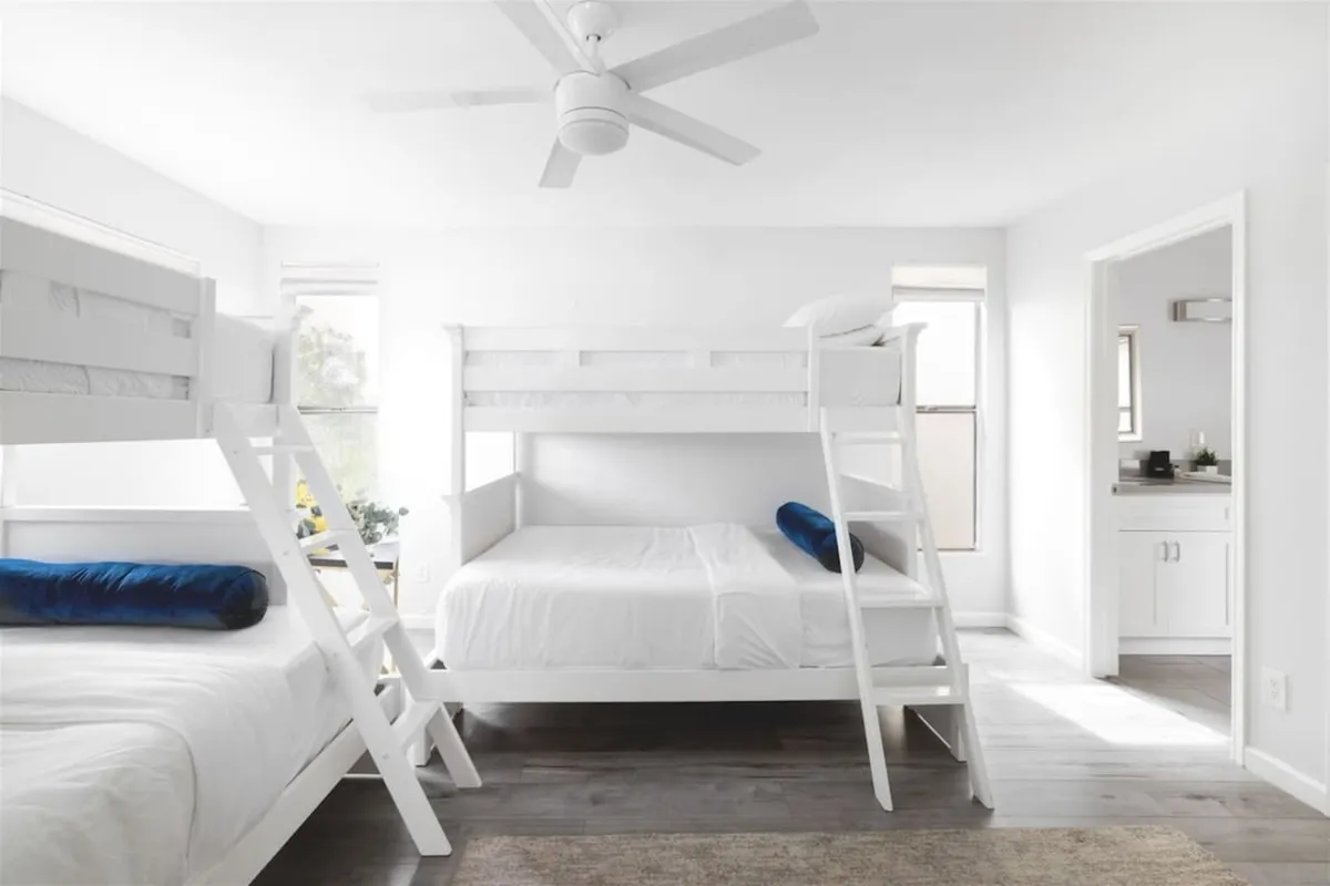 A playful kids’ bunk room featuring stacked bunk beds, an additional single bed, a window with soft lighting, and an open bathroom door. The atmosphere is cheerful and relaxed, inviting bedtime stories or playtime for younger guests.