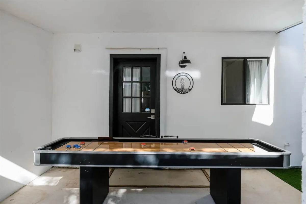 The photo focuses on an air hockey table set against a bold wall with a logo, suggesting a dedicated space for friendly competition and socializing. The room's design is casual and inviting, perfect for enjoying memorable game nights with friends or family.